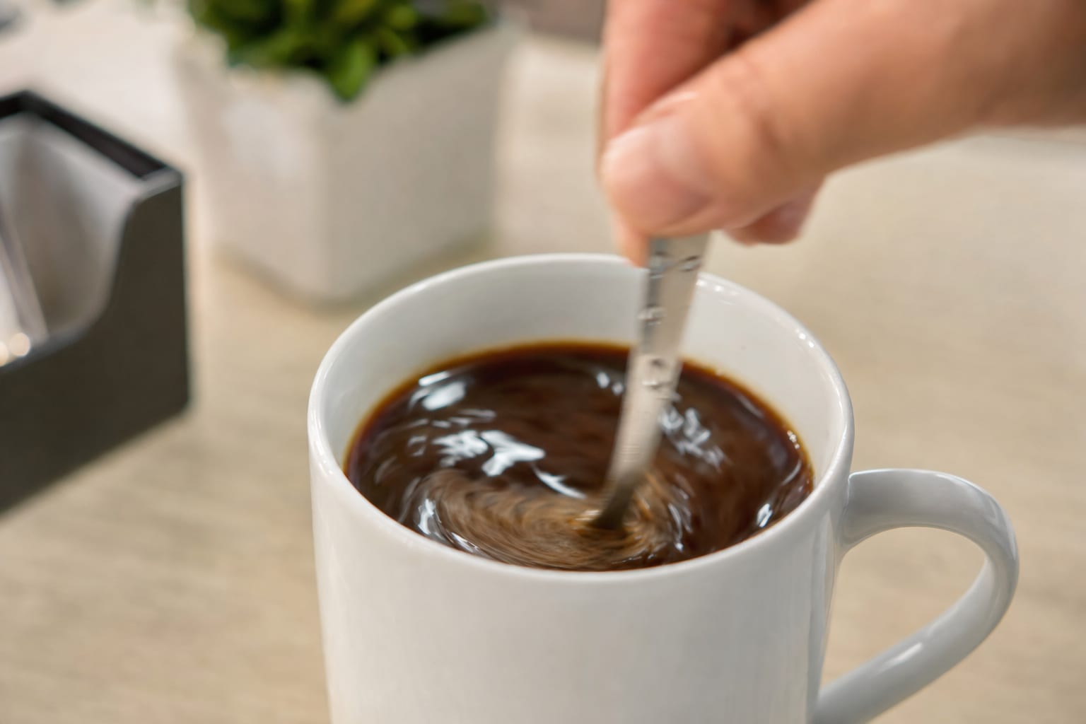 close-up-de-uma-mao-mexendo-cafe-soluvel-em-uma-caneca-branca-com-uma-colher-des